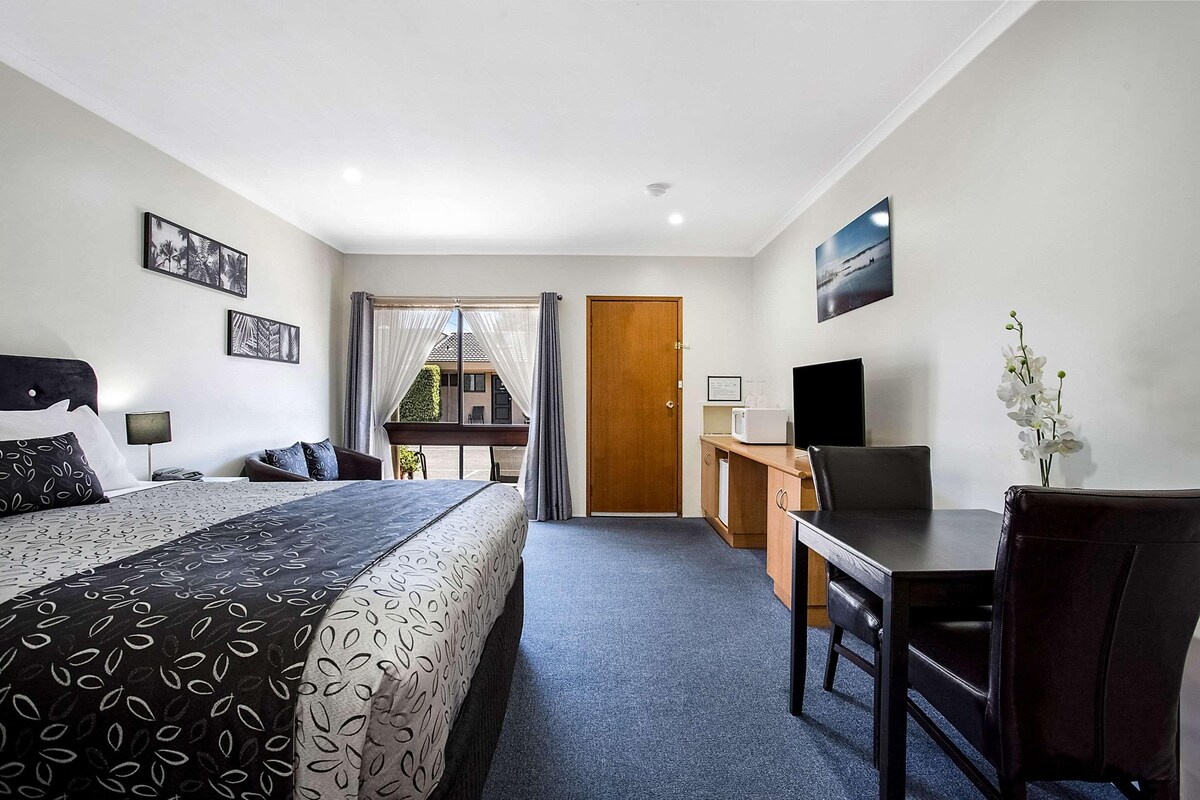 Habitación de hotel con cama, escritorio, silla y vista al exterior.