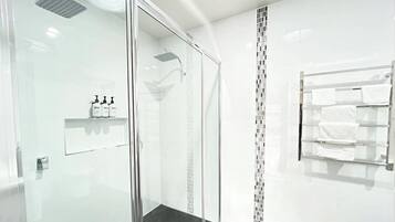 A modern bathroom with a glass-enclosed shower, a towel rack, and a shelf with toiletries.