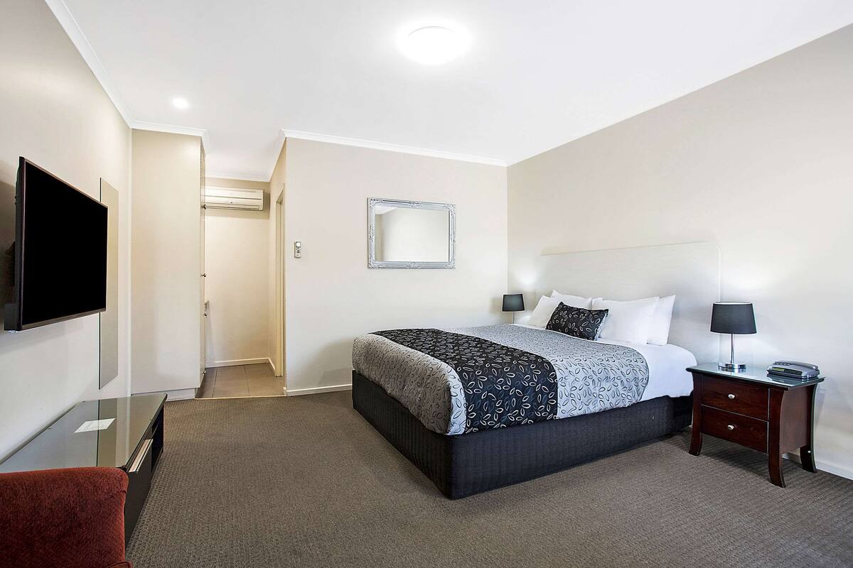 A hotel room with a bed, bedside tables, a TV, and a mirror.
