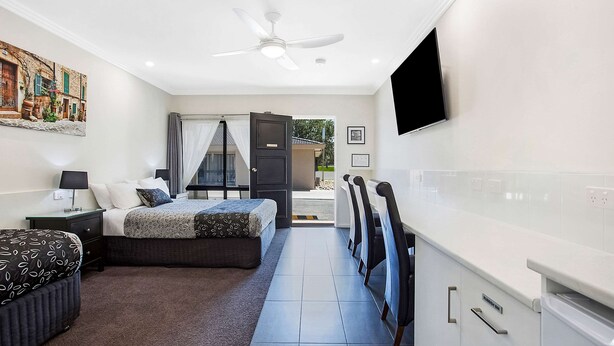 Una habitación de hotel moderna con cama, mesitas de noche, televisor de pantalla plana, ventilador de techo y vistas al exterior.