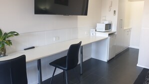 Cocina moderna con televisor de pantalla plana, microondas y pileta. Hay dos sillas negras y una planta en maceta.
