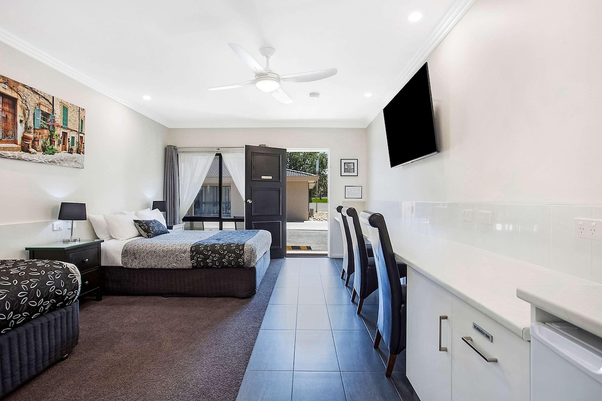 Una habitación de hotel moderna con una cama, mesitas de noche, ventilador de techo y televisor montado en la pared.