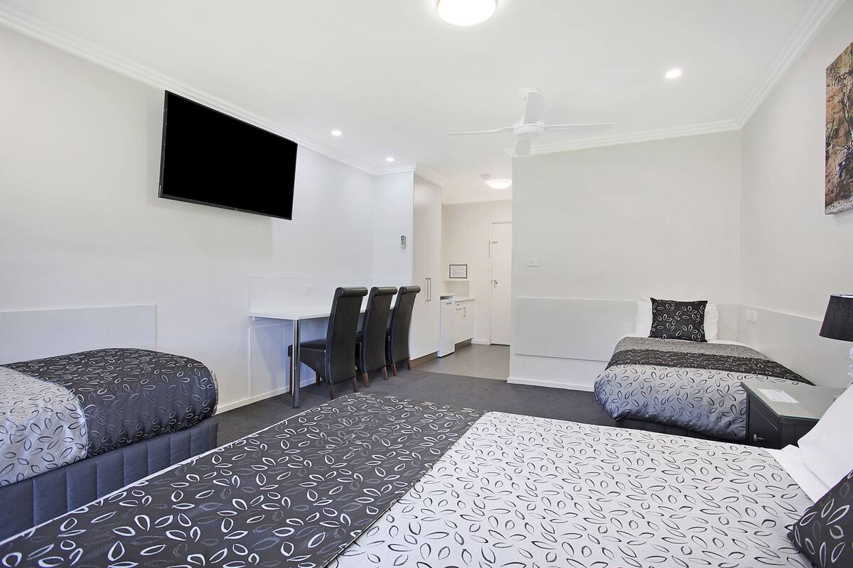 A hotel room with two beds, a desk, chairs, a flat-screen TV, and a ceiling fan.