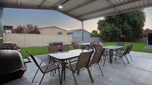 Un patio al aire libre con zona de estar cubierta, una parrilla y un césped bien cuidado.