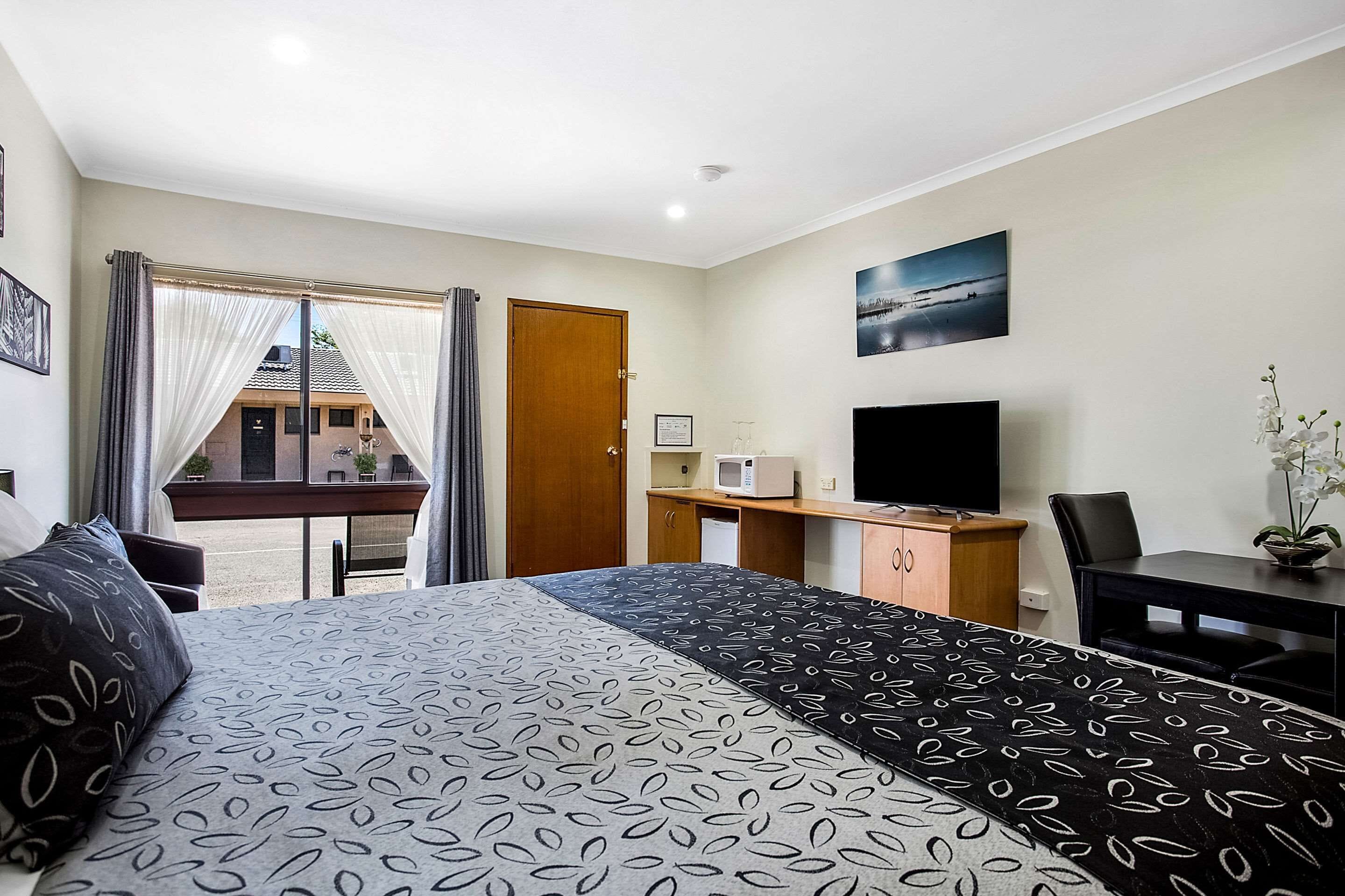 Habitación de hotel con cama, escritorio, televisor y vistas al exterior.