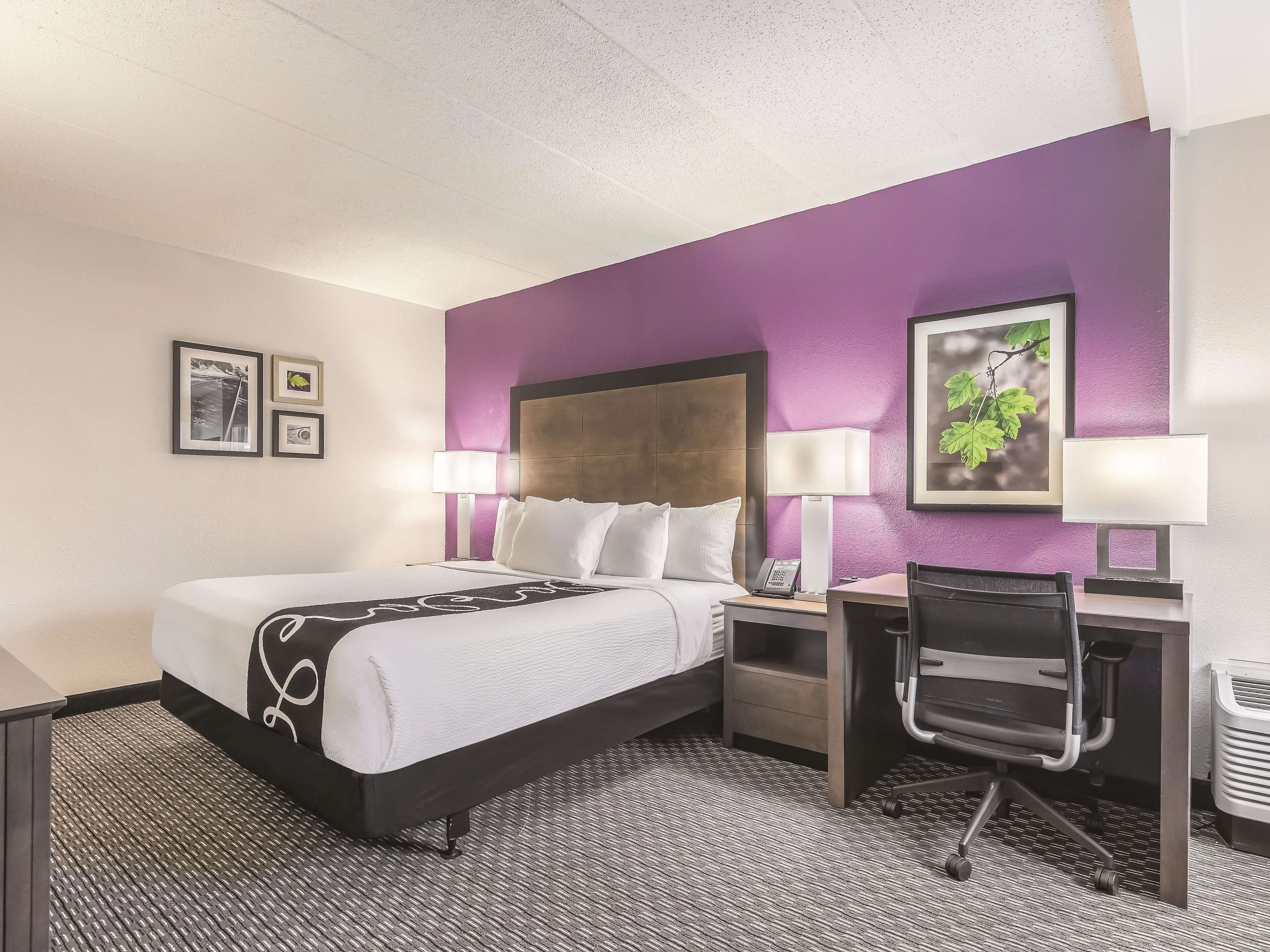 A hotel room with a bed, desk, chair, and two bedside lamps.