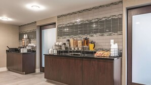 A modern hotel lobby with a reception desk, a coffee station, and a tiled backsplash.