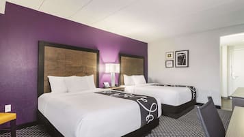 A hotel room with two beds, a desk, a chair, and a lamp.