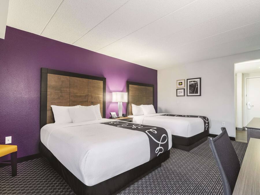 A hotel room with two beds, a desk, a chair, and a lamp.