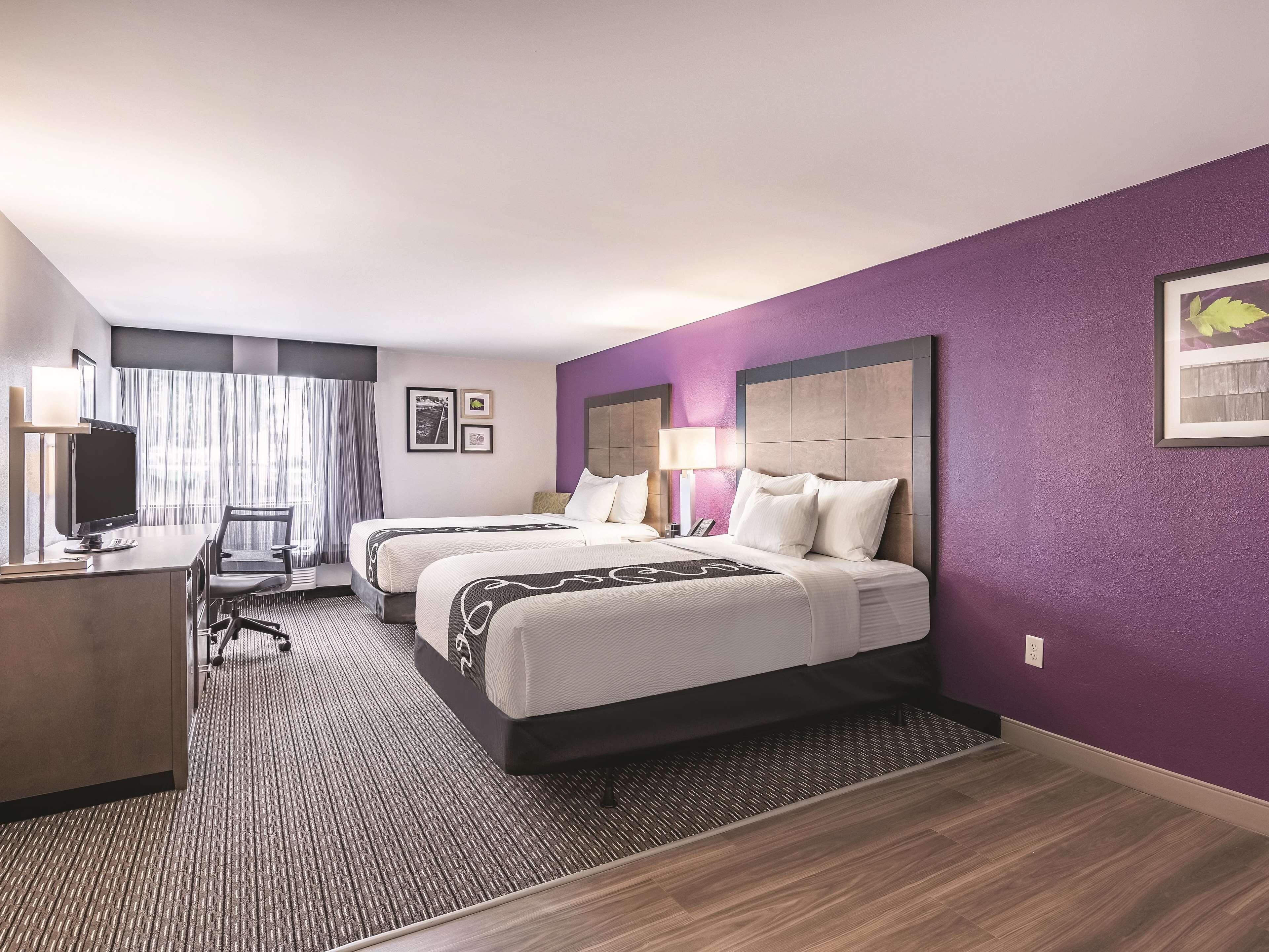 A hotel room with two beds, a desk with a computer, and a window with curtains.