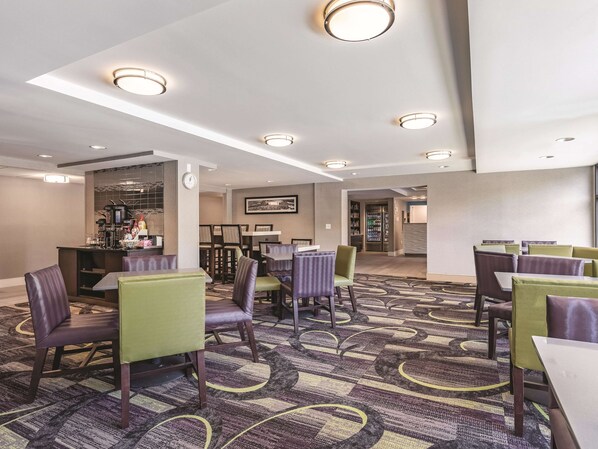 A hotel lobby with multiple seating areas, a bar, and a refrigerator stocked with beverages.