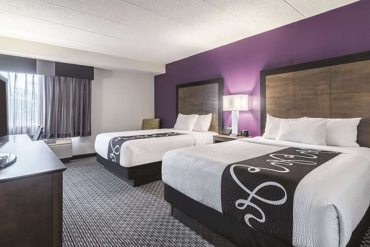 A hotel room with two beds, a desk, and a window with curtains.
