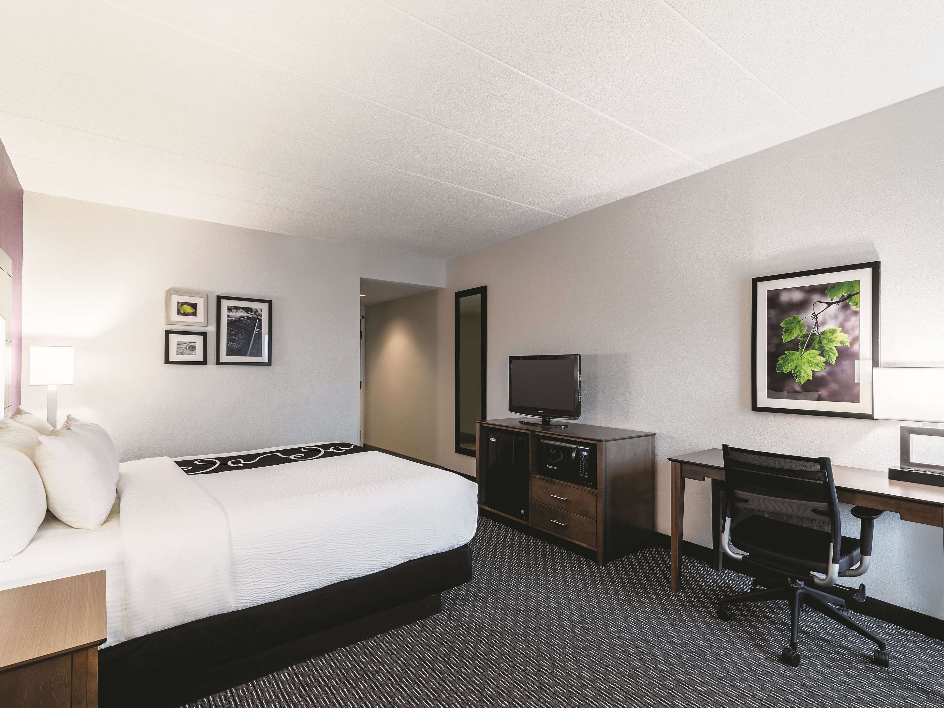 Una habitación de hotel con cama, escritorio, silla, televisor y cuadros en la pared.