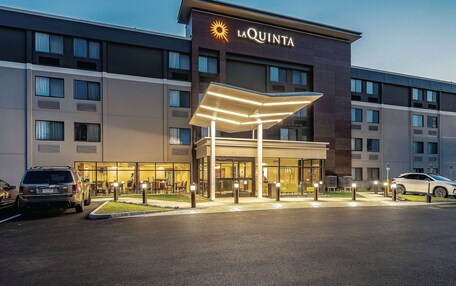 A hotel with a prominent 'La Quinta' sign, a covered entrance, and a parking area with cars.
