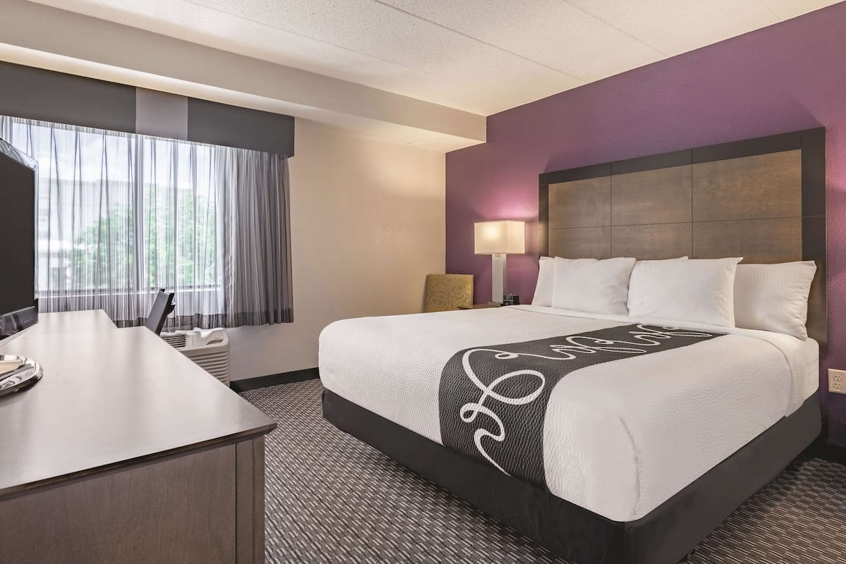 A hotel room with a bed, a desk, a chair, a lamp, and a window with curtains.