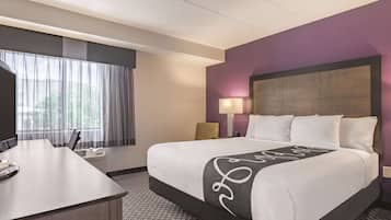 A hotel room with a bed, a desk, a chair, a lamp, and a window with curtains.