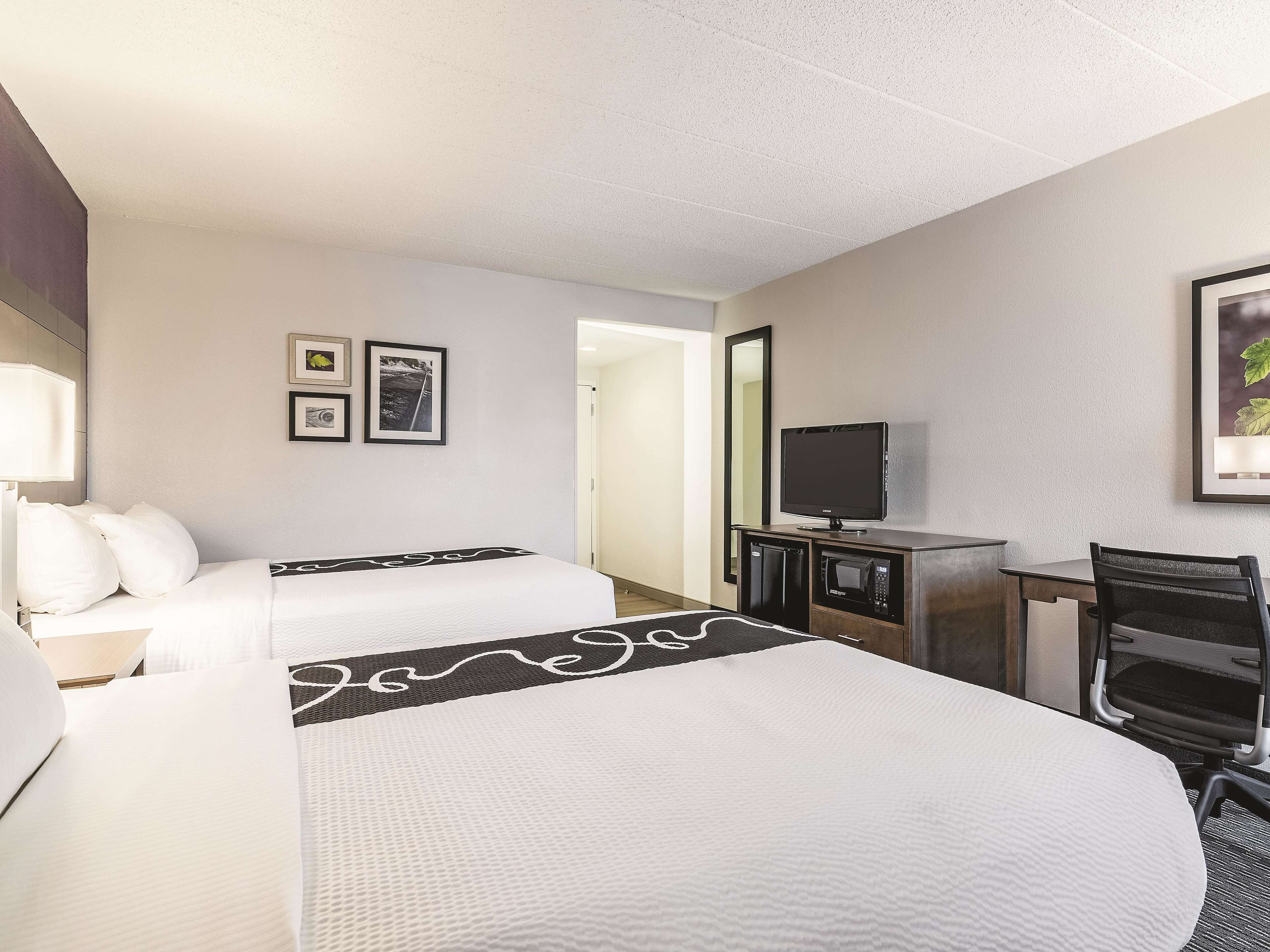 A hotel room with two beds, a desk with a TV, a microwave, and a chair.