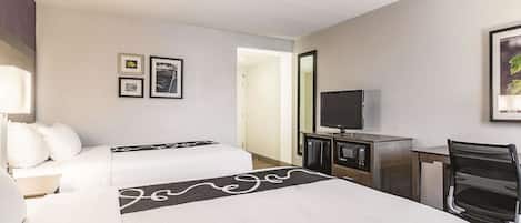 A hotel room with two beds, a desk with a TV, a microwave, and a chair.
