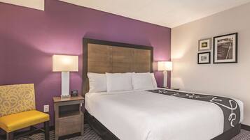 A hotel room with a bed, two bedside lamps, a nightstand, a chair, and a wall with framed pictures.