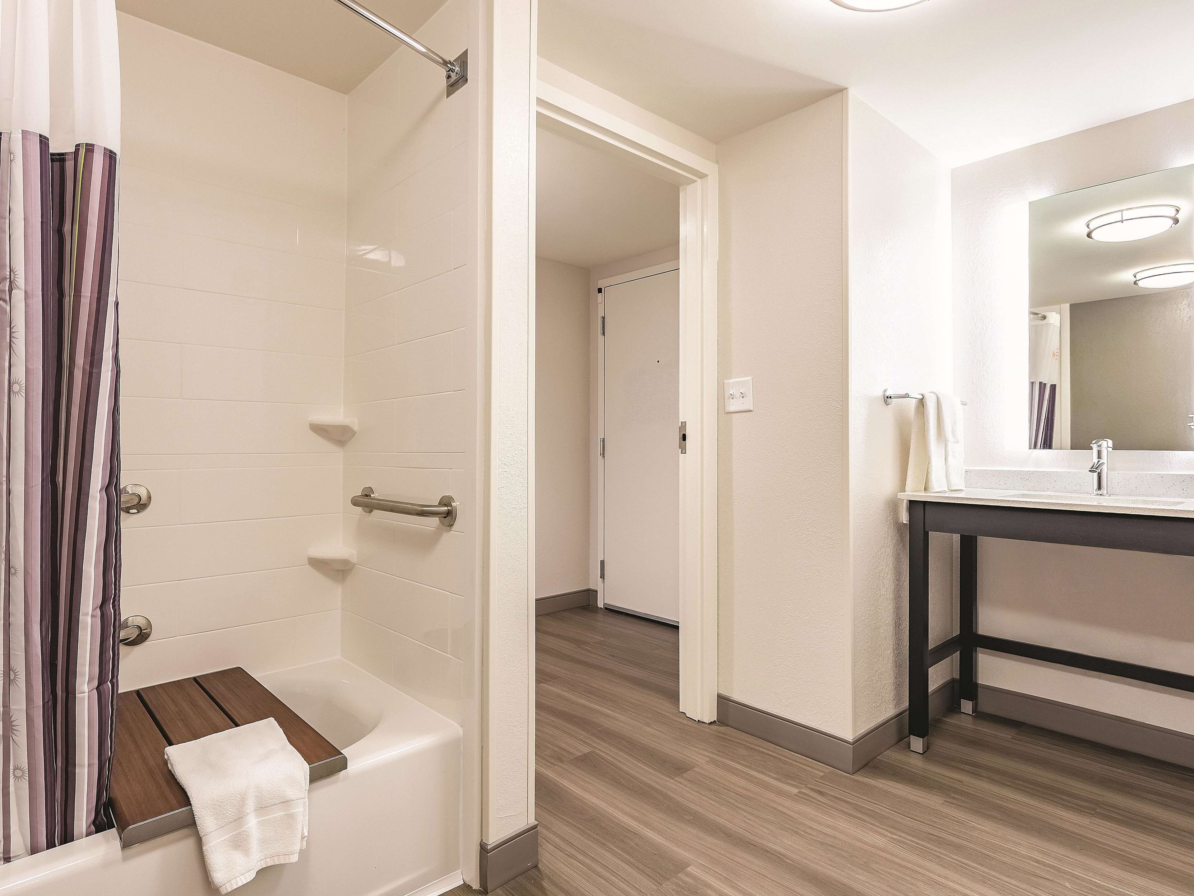 A bathroom with a shower, a wooden bench, a towel, a sink, and a mirror.