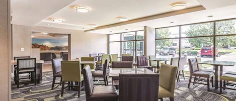 A hotel lobby with multiple seating areas, large windows, and a carpeted floor.