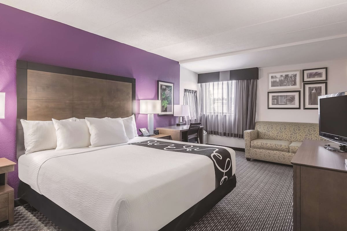 A hotel room with a large bed, a desk with a chair, a television, and framed pictures on the wall.