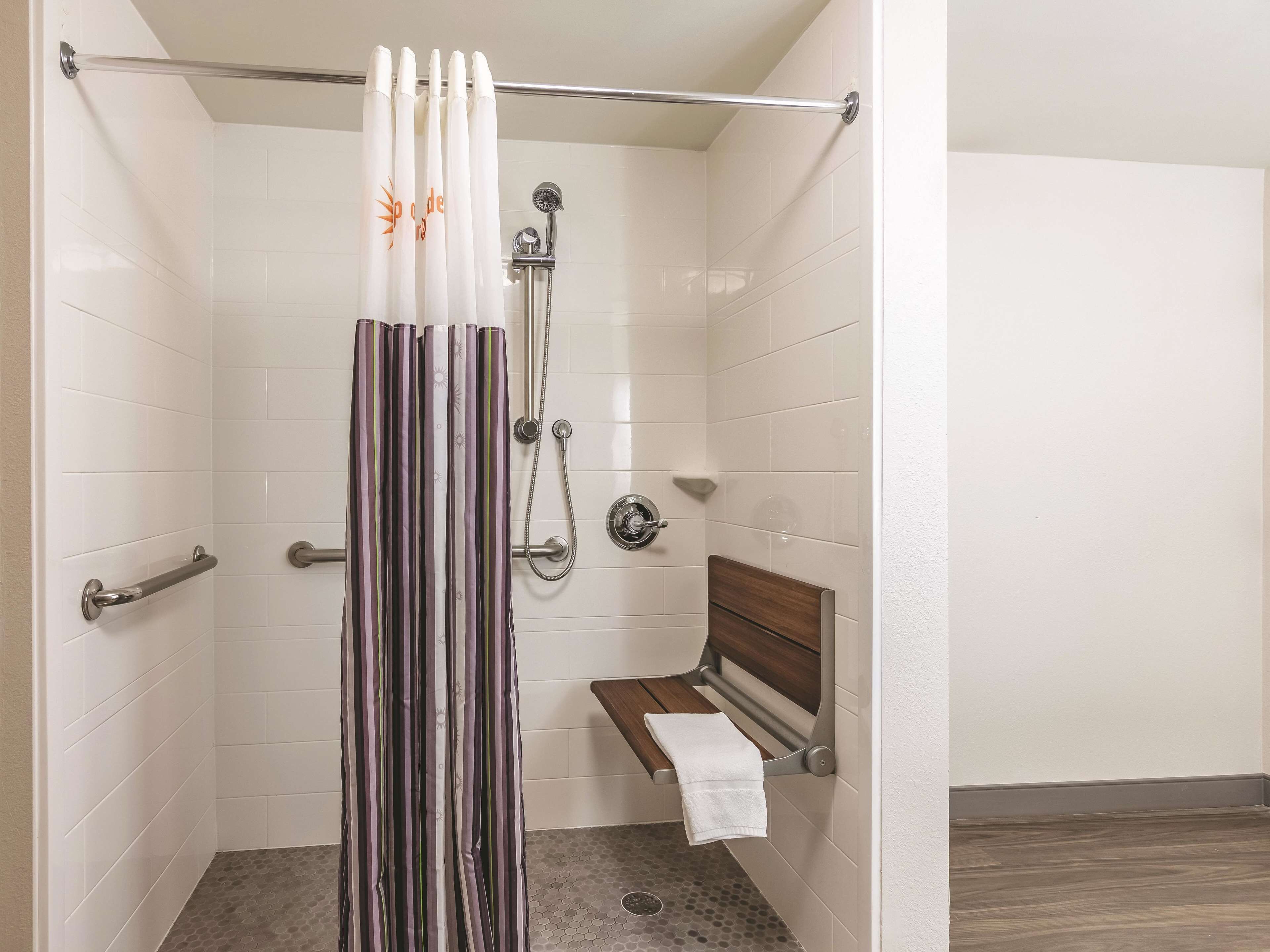 A shower with a striped curtain, a handheld showerhead, and a wooden bench with a towel.