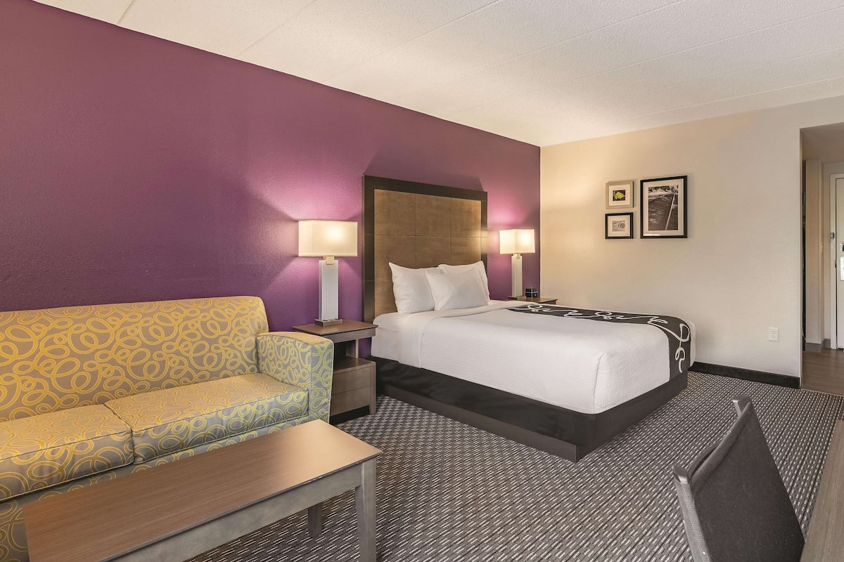 A hotel room with a bed, a sofa, two bedside tables with lamps, and a carpeted floor.