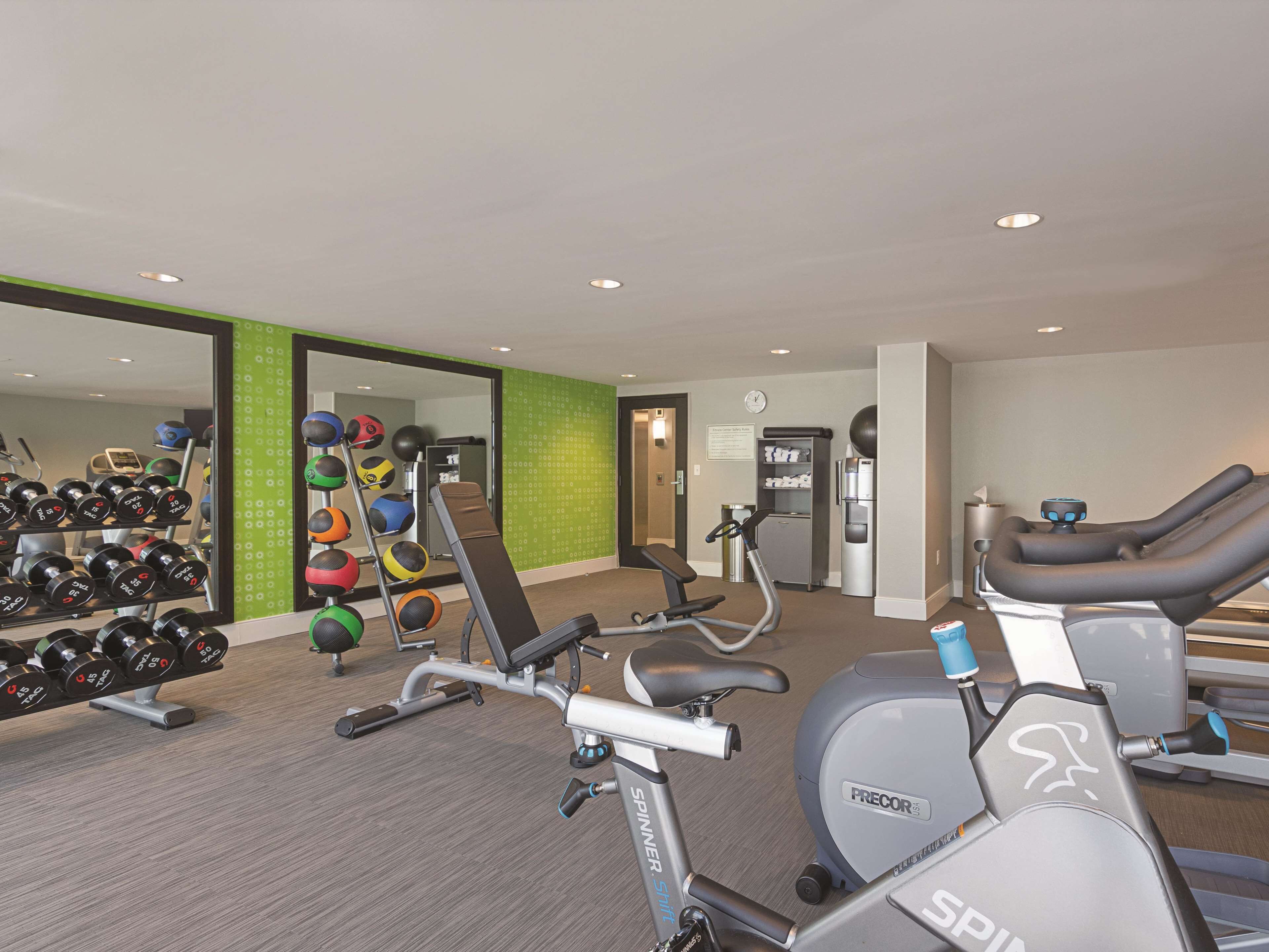 Un gimnasio con equipo de ejercicio, incluyendo mancuernas, una banca y máquinas de cardio.