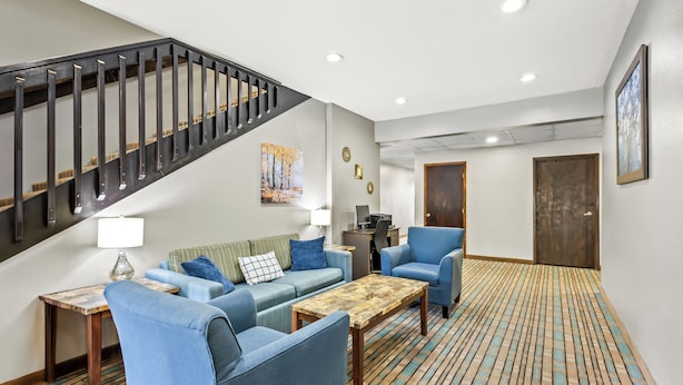 Ein modernes Wohnzimmer mit Treppe, blauem Mobiliar, einem Holztisch und einem gemusterten Teppich.