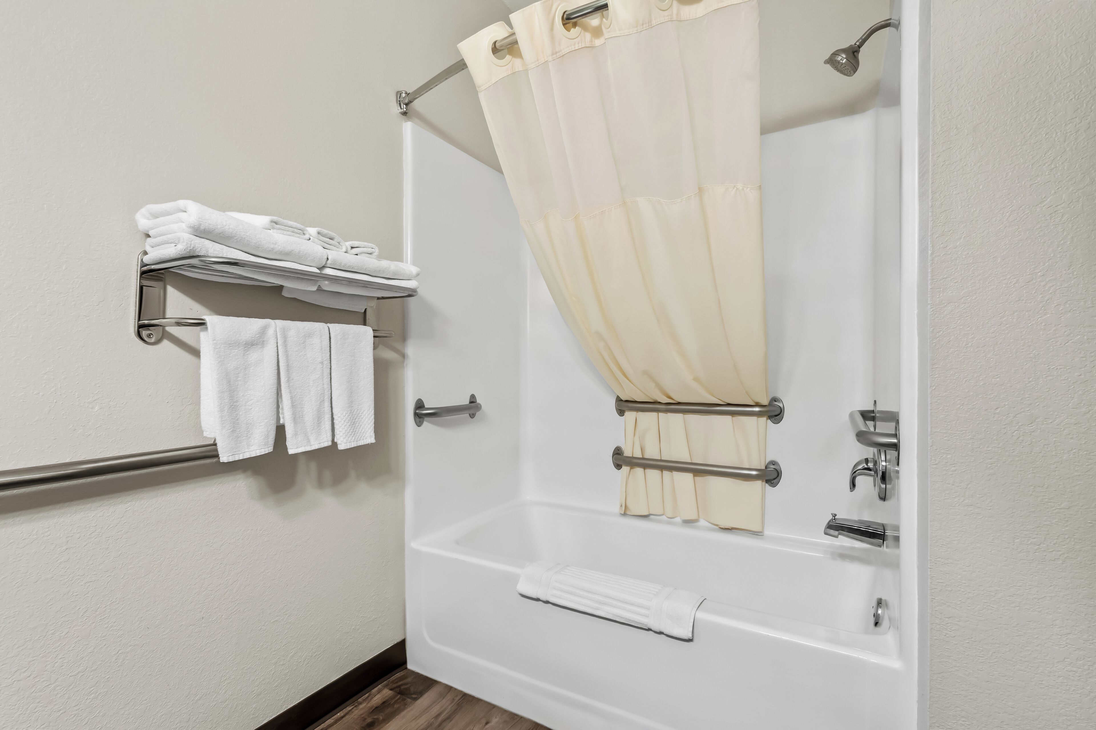 Une salle de bain avec une baignoire, un rideau de douche, un porte-serviettes avec des serviettes pliées et une pomme de douche.