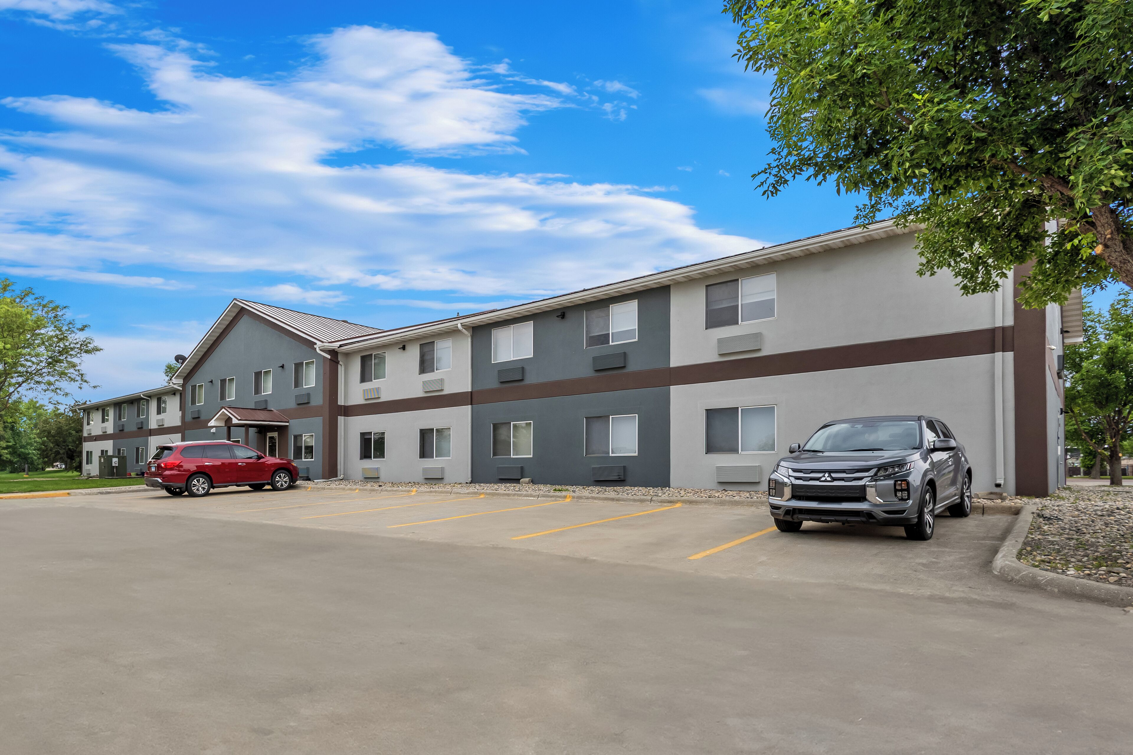 A multi-story building with a parking lot, a red car, and a silver SUV.