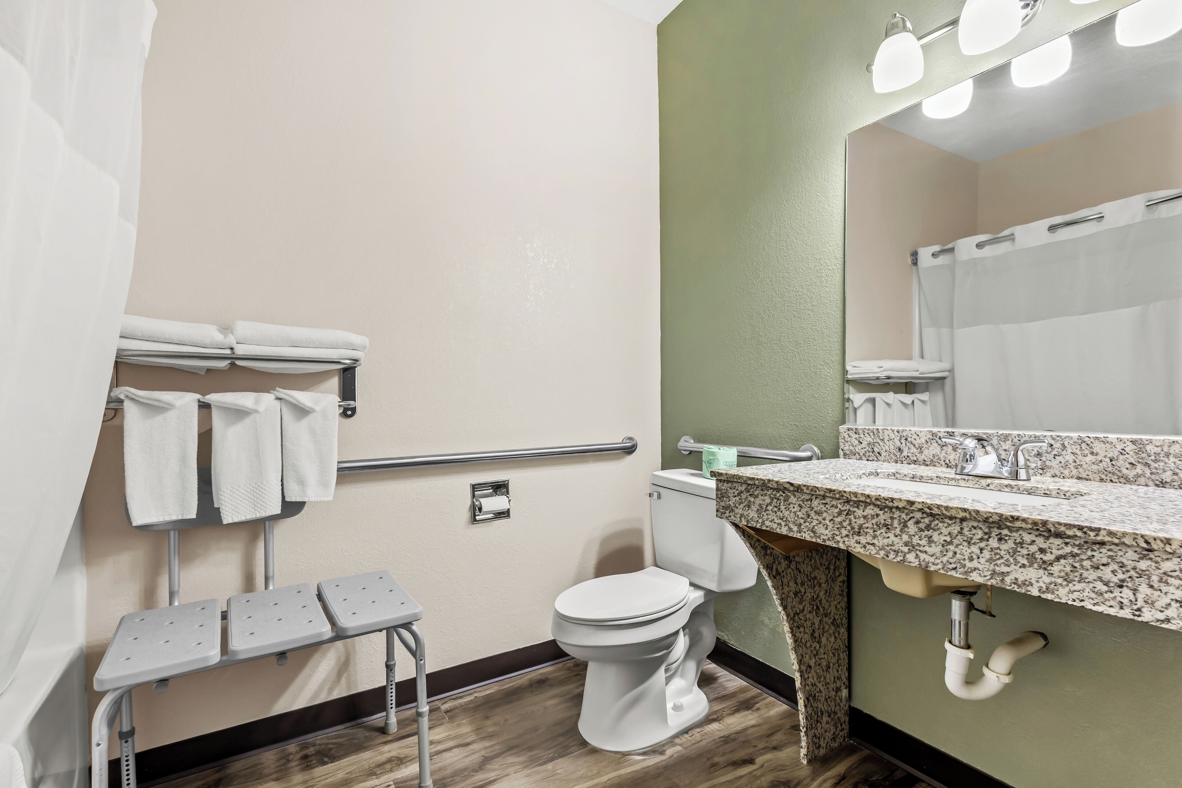 Un baño con inodoro, lavabo, espejo, toallero y un banco.