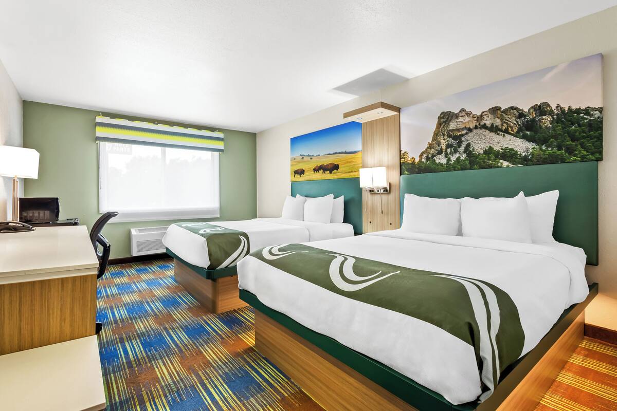 A hotel room with two beds, a desk, a chair, and a large window.