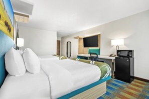 A hotel room with a bed, desk, chair, and a small refrigerator.