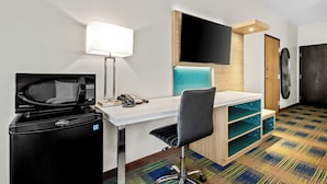 Ein kompaktes Hotelzimmer mit Küchenzeile, einem Schreibtisch mit Stuhl, einem flachbildfernseher an der Wand und einer Waschmaschine.