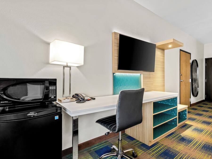 Habitación de hotel compacta con kitchenette, un escritorio con silla, un televisor de pantalla plana montado en la pared y una lavadora.