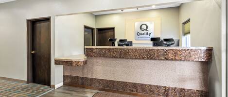 Una mesa de recepción con un cartel de 'Quality by Choice Hotels', un mostrador de registro y un área de espera con un tapete marrón.