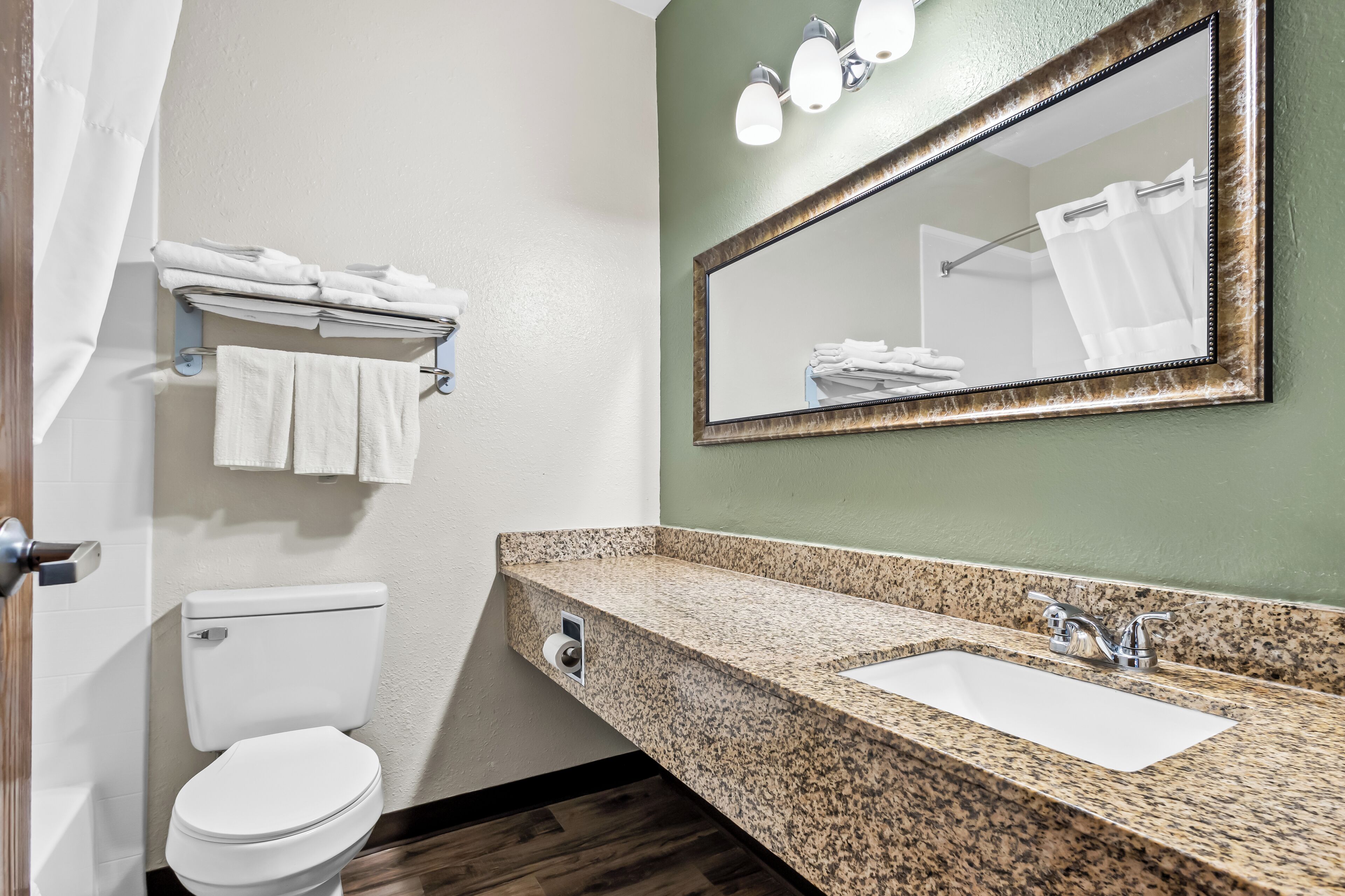 A bathroom with a white toilet, a granite countertop sink, a mirror, and a towel rack.