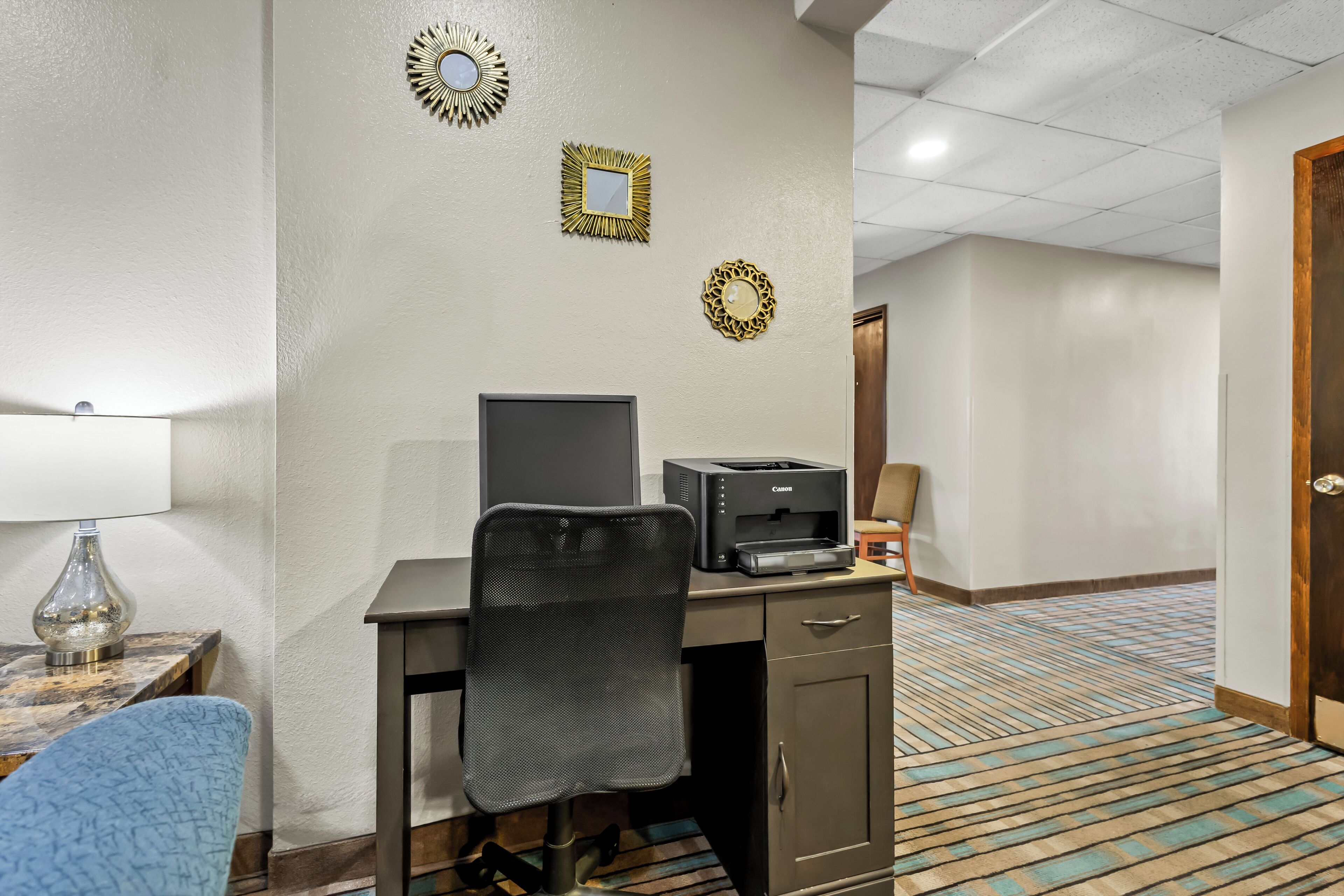 A hotel room with a desk, chair, printer, lamp, and decorative wall mirrors.