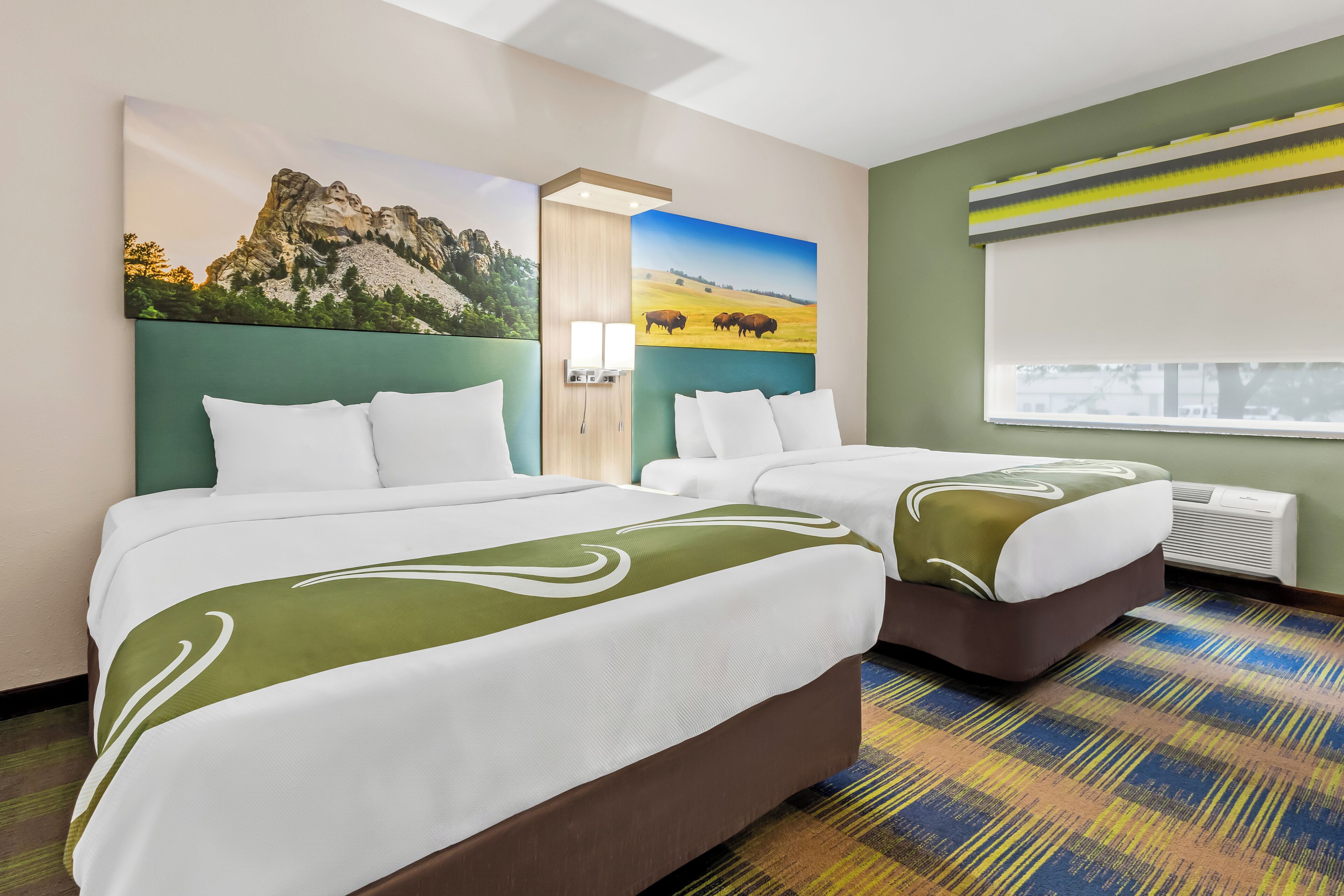 A hotel room with two beds, a large window, and a painting of a mountain and field.