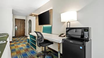 Habitación de hotel con escritorio, silla, televisor de pantalla plana, microondas y refrigerador.