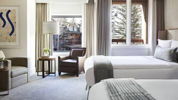 A hotel room with a large bed, a chair, a small table with a lamp, and a view of a snowy landscape through the window.