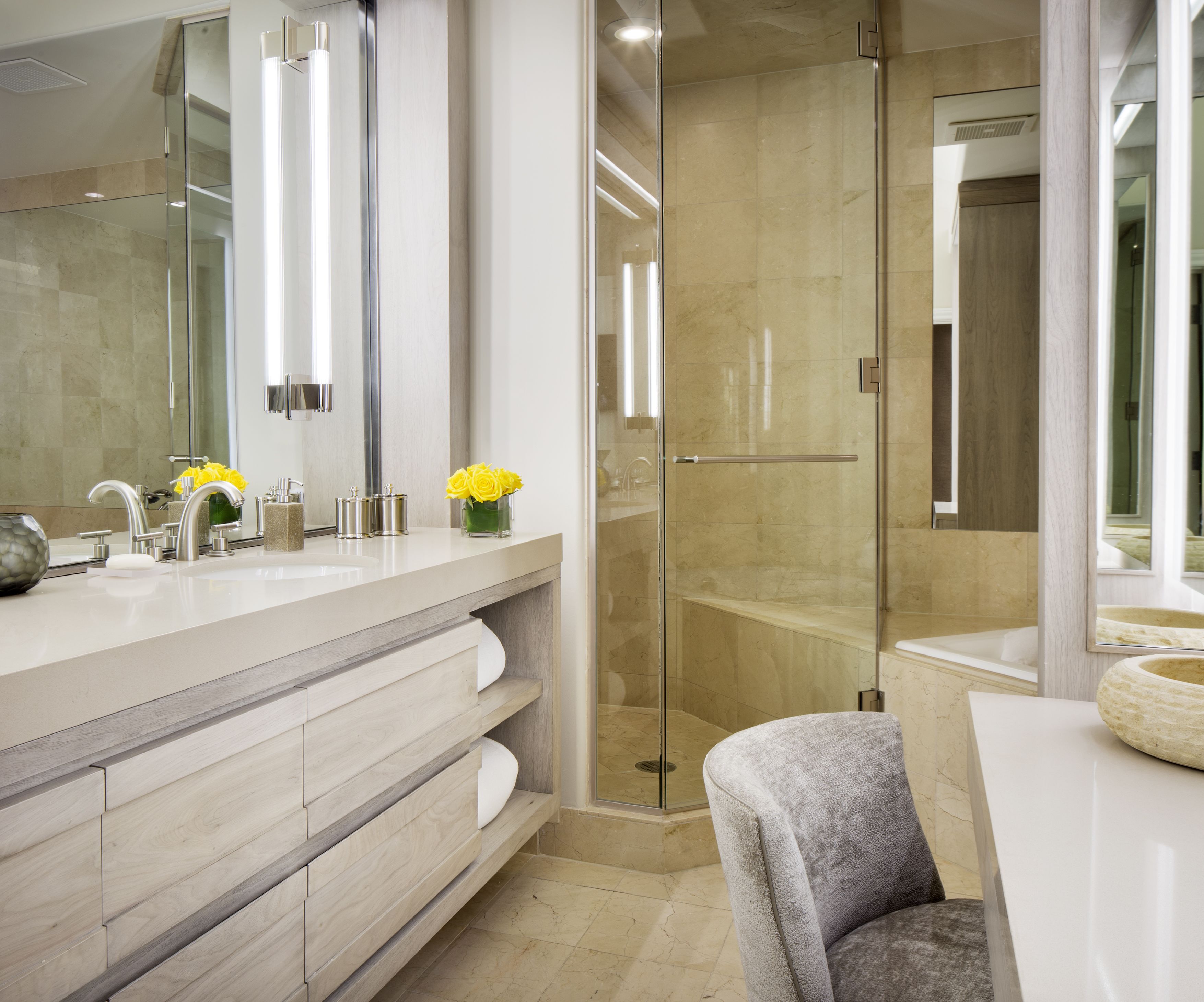 A modern bathroom with a glass-enclosed shower, a large mirror, and a vanity with a marble countertop.