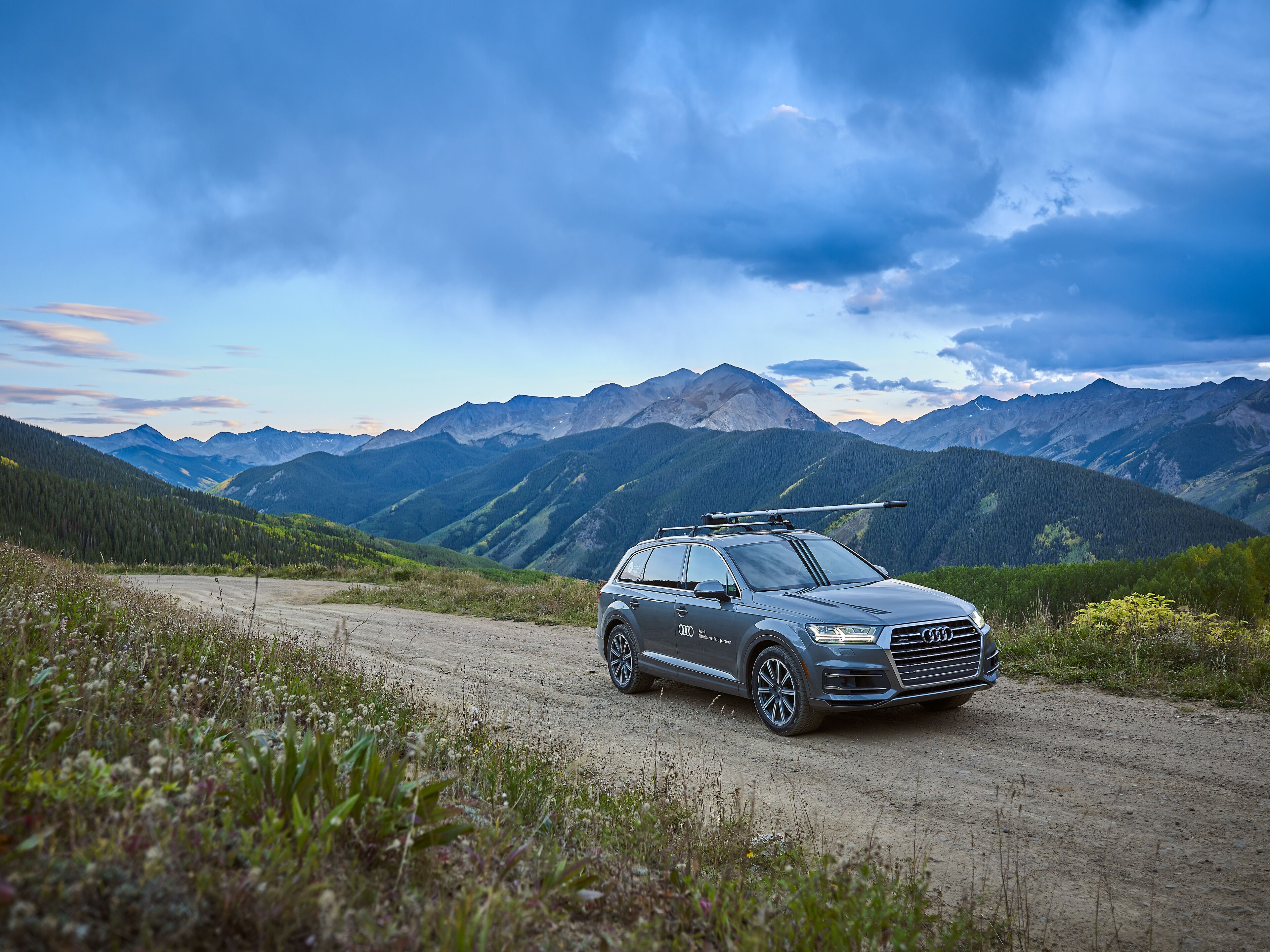Un coche aparcado en un camino de tierra con un paisaje montañoso al fondo.