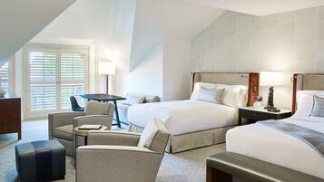 A hotel room with two beds, a desk, a chair, and a small table.