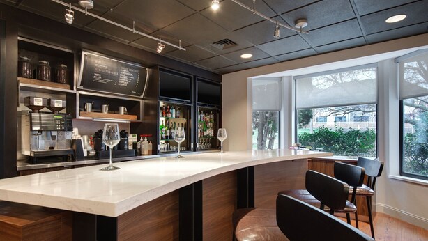 A modern bar area with a curved counter, bar stools, and a menu board. - Courtyard by Marriott State College (State College)