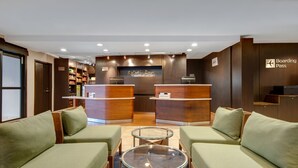 A reception area with two wooden reception desks, a glass-top table, and green upholstered sofas. - Courtyard by Marriott State College (State College)