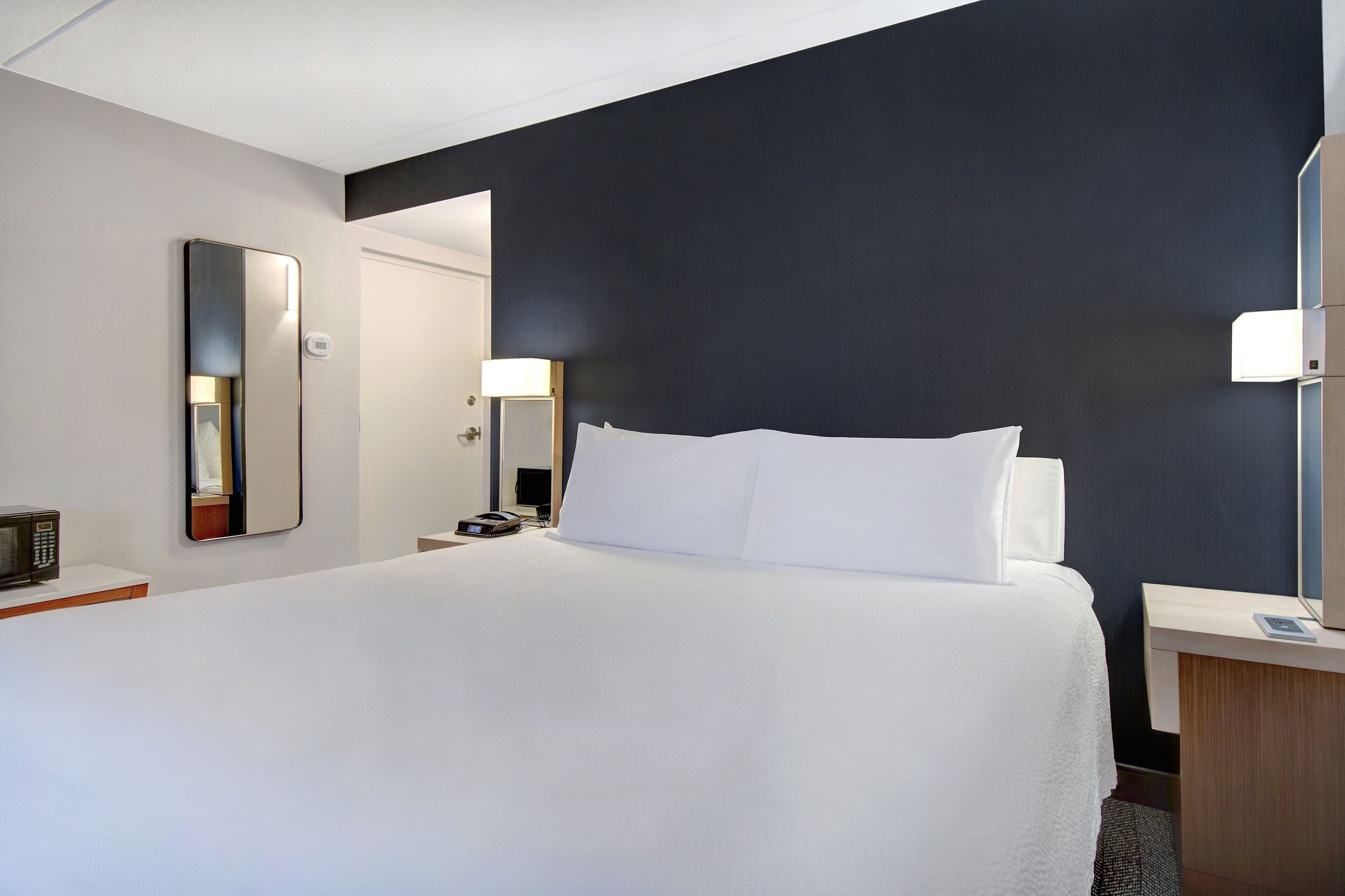 A hotel room with a large bed, bedside tables, a mirror, and a nightstand.