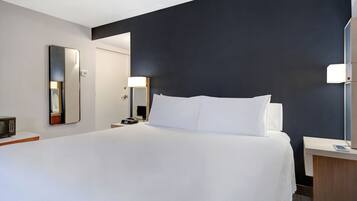 A hotel room with a large bed, bedside tables, a mirror, and a nightstand.